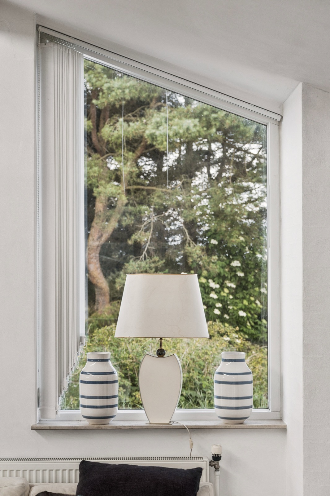 Vindueskarm med bordlampe og stribede keramikvaser mod en grøn have.
