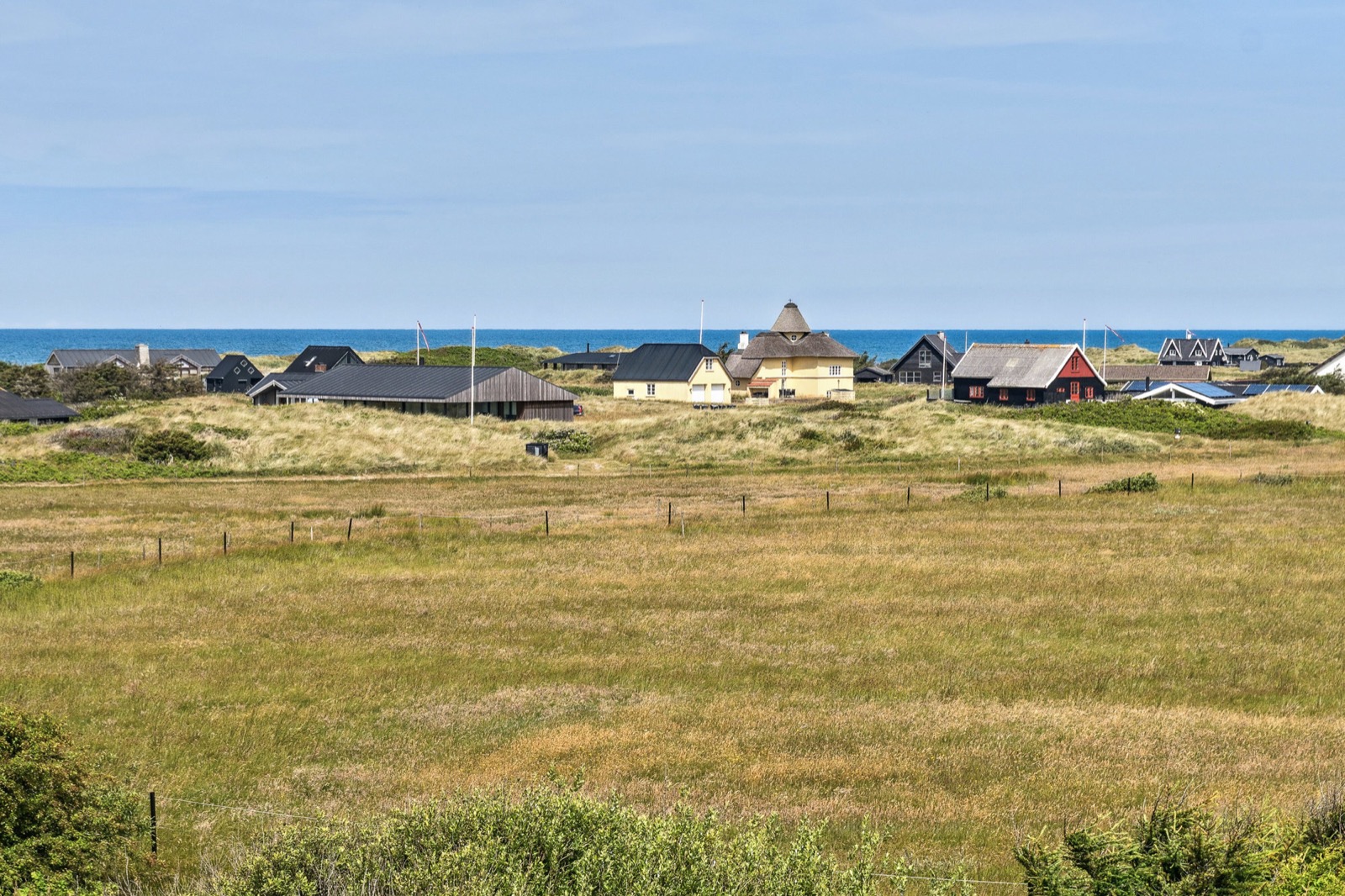 Panorama fra klittoppen over Blokhus-kysten med havhorisont, stråtækte huse og sorttjærede huse.
