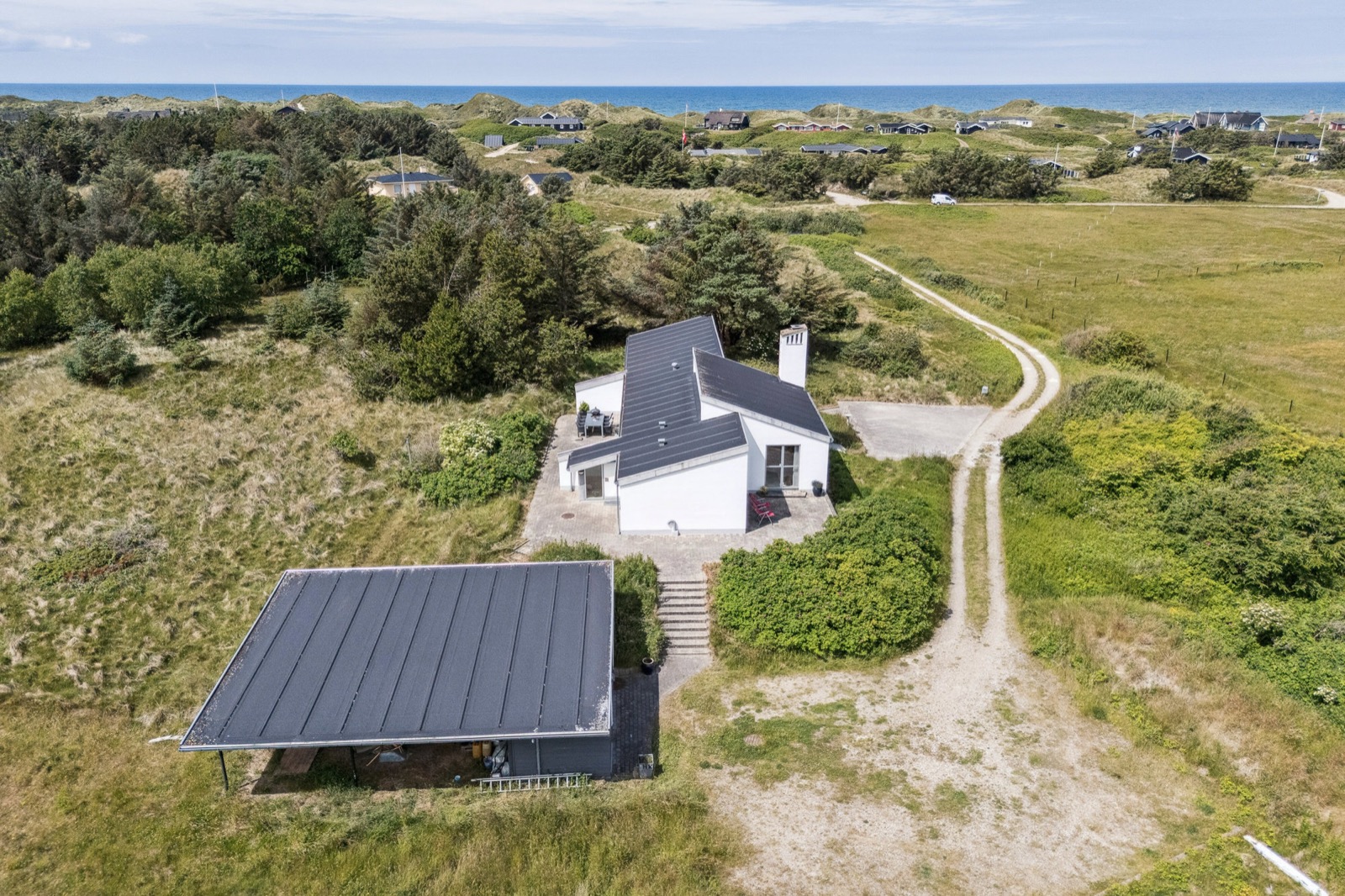 Dronefoto af huset og garagen med hav og Blokhus i horisonten.